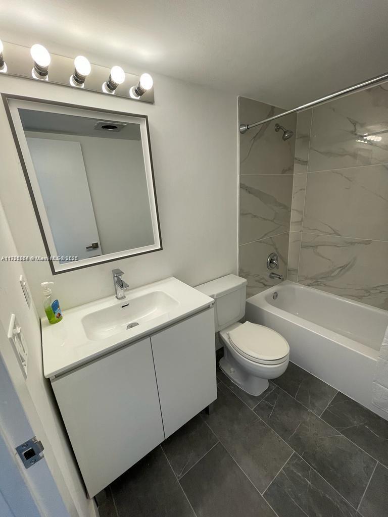 A modern bathroom features a white vanity, a rectangular mirror, and a tiled bathtub shower — 22 Suffolk A # 22, Boca Raton FL 33434, BOCA RATON, FL