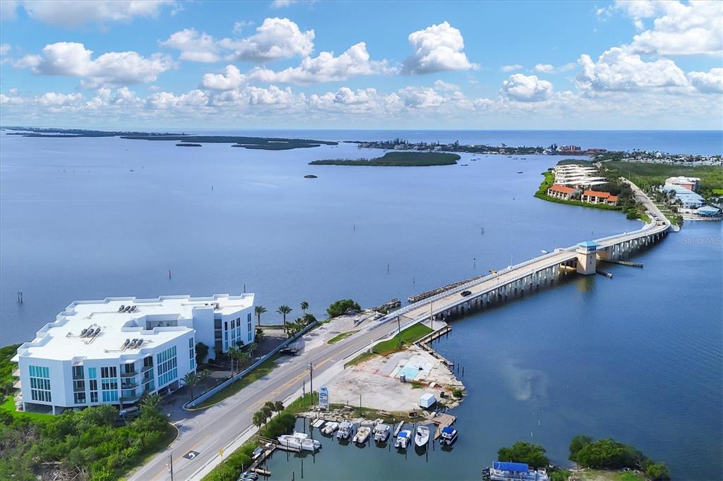 An aerial view shows a white multi-story building next to a bridge over water — 1375 BEACH ROAD UNIT 311, ENGLEWOOD, FL