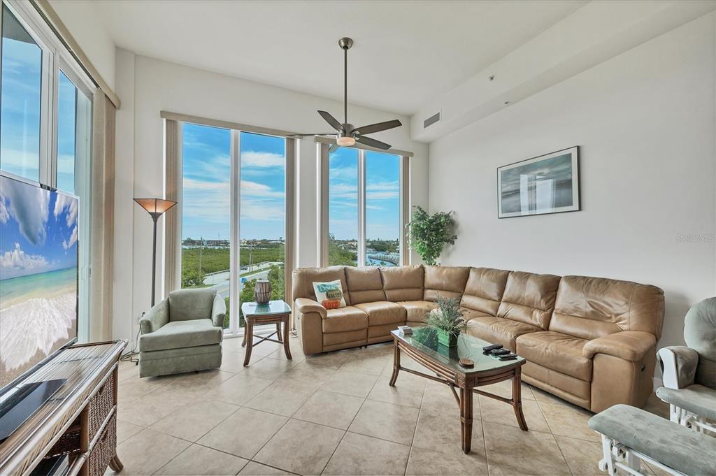 A living room features a tan leather sectional, tile flooring, and floor-to-ceiling windows with water views — 1375 BEACH ROAD UNIT 311, ENGLEWOOD, FL