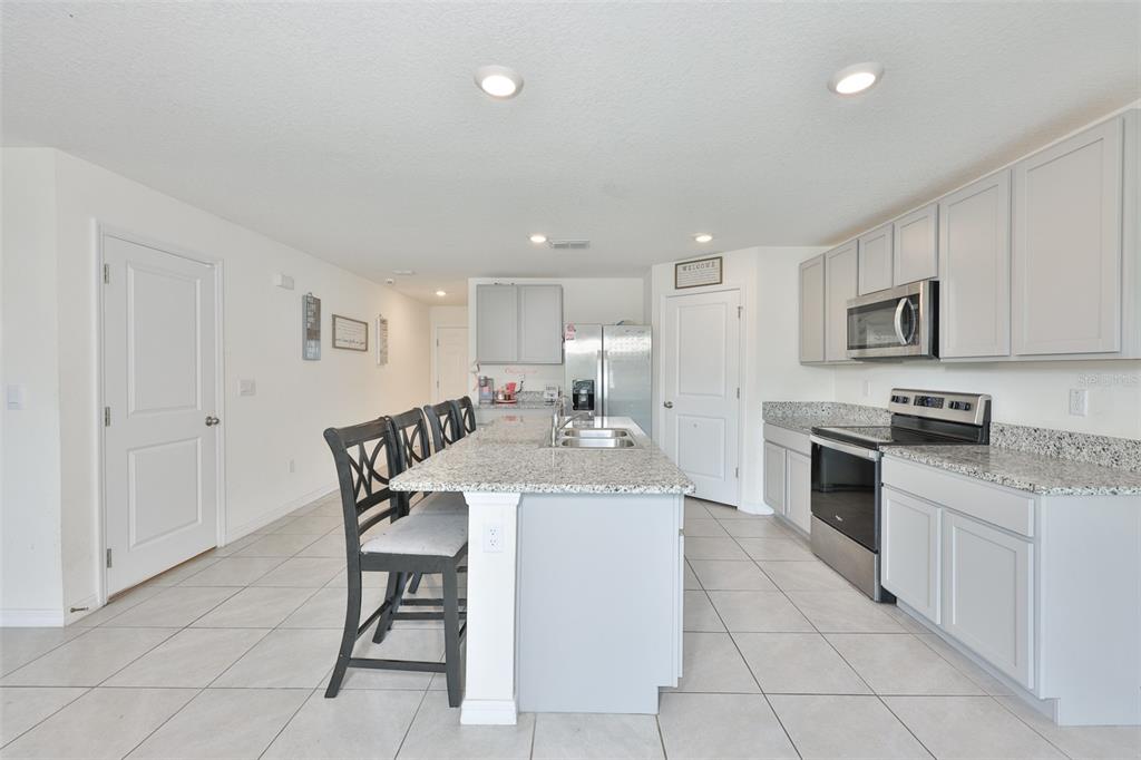 A kitchen features light gray cabinets, granite countertops, a central island, and stainless steel appliances — 5244 FIDDLE FIG AVENUE, WIMAUMA, FL
