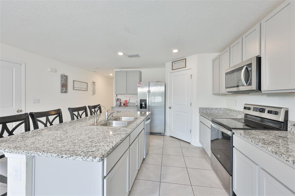 A kitchen features light gray cabinets, granite countertops, stainless steel appliances, and a central island — 5244 FIDDLE FIG AVENUE, WIMAUMA, FL