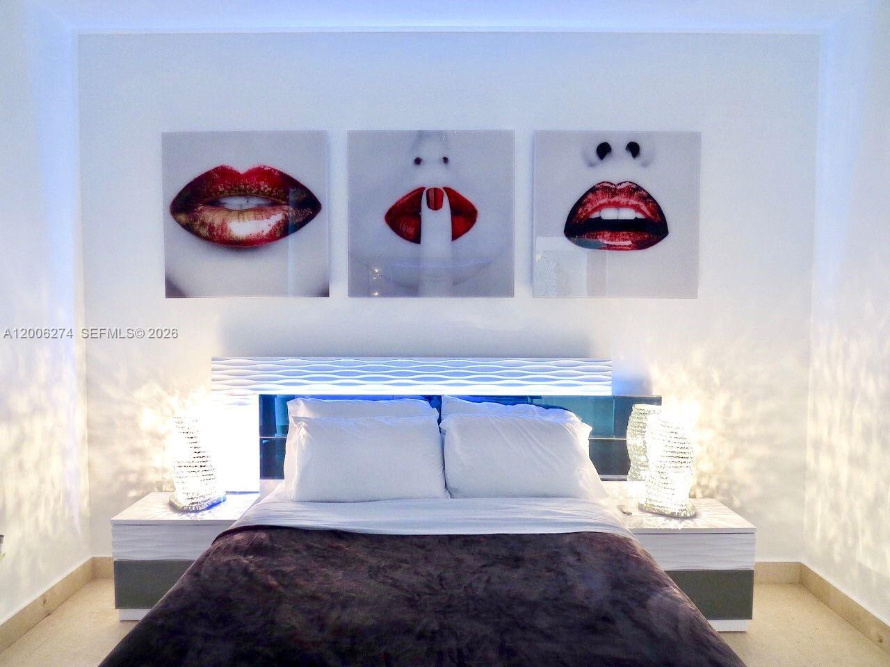 A bedroom features a bed with white pillows, a dark blanket, and three lip-themed artworks — 465 Brickell Ave # 5704, Miami FL 33131, MIAMI, FL