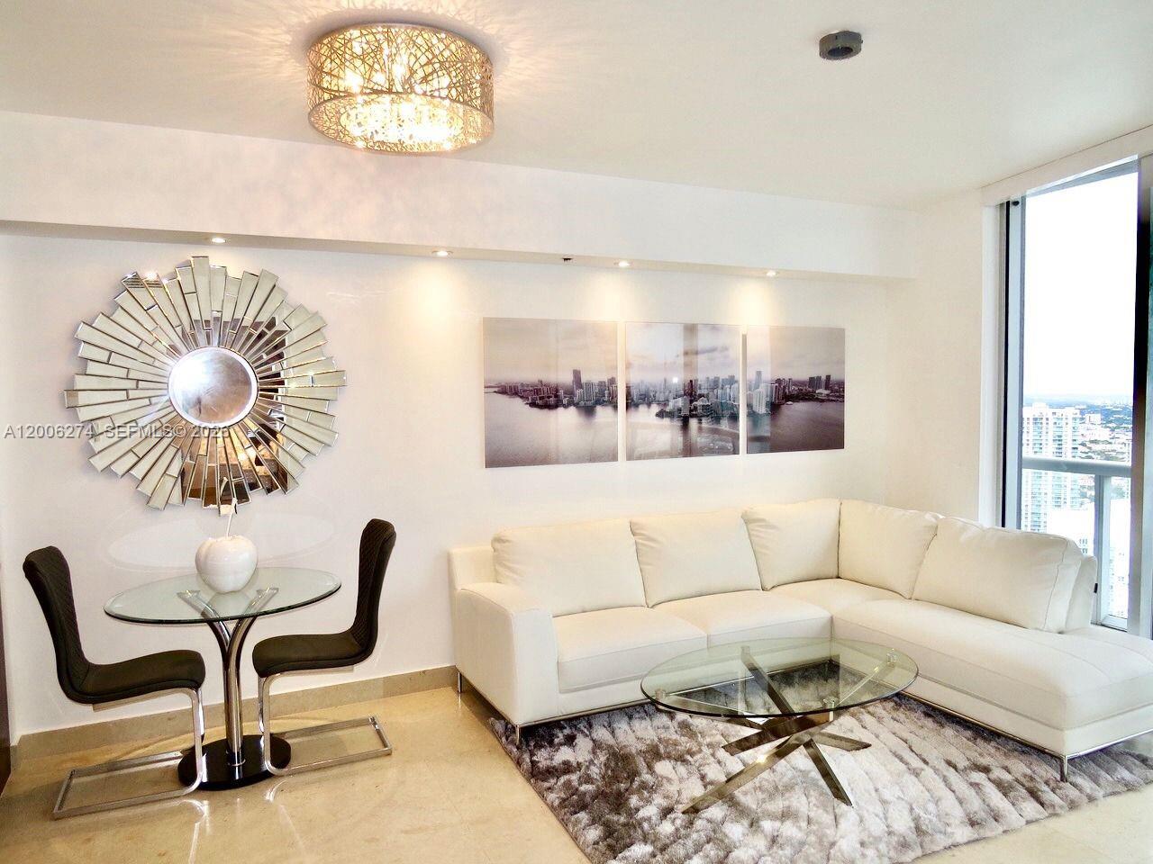 A modern living and dining area features a white sectional sofa, glass tables, and wall art — 465 Brickell Ave # 5704, Miami FL 33131, MIAMI, FL