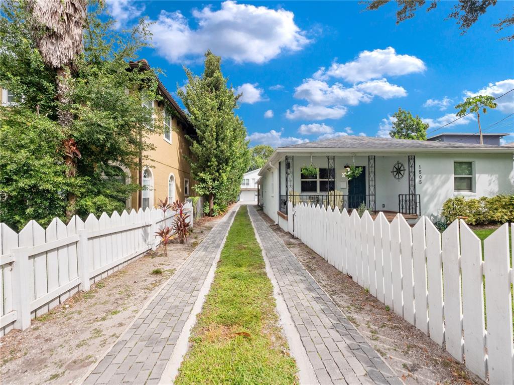 A paved driveway with a grass strip leads between two houses with white picket fences — 1505 CATHERINE STREET, ORLANDO, FL
