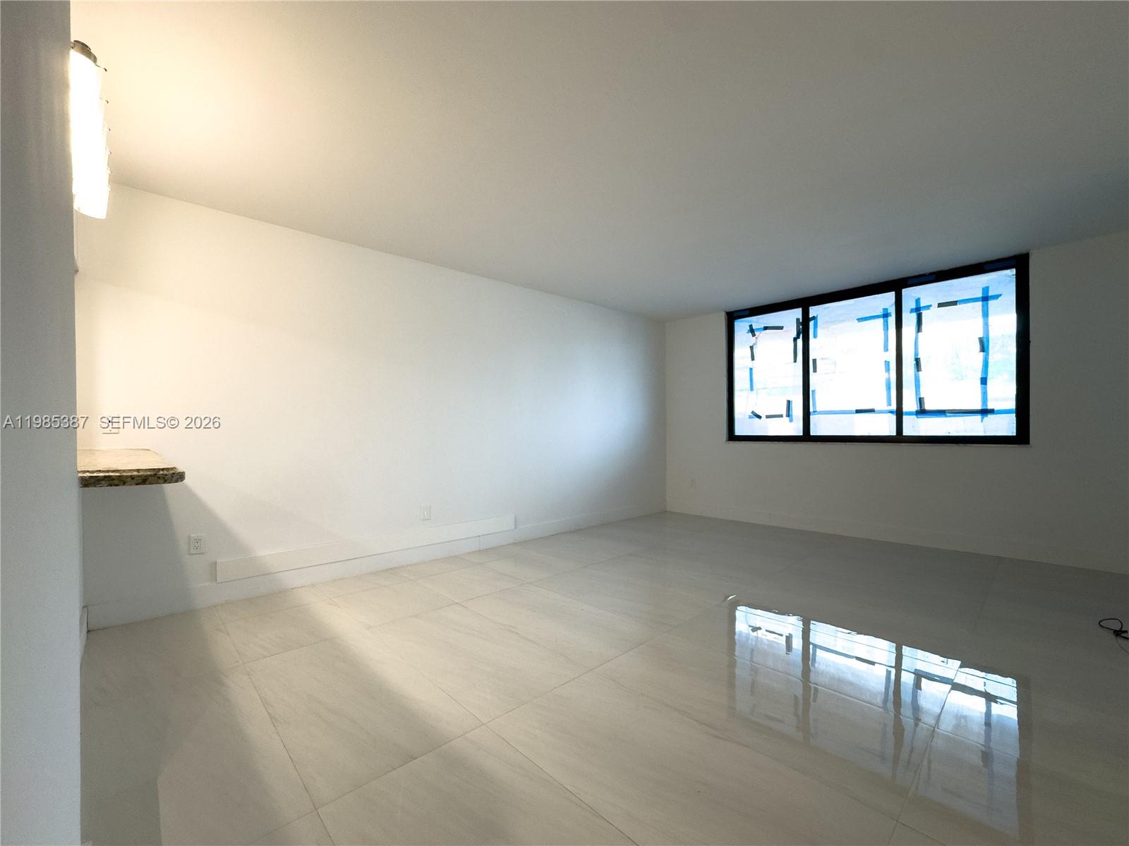 An empty room features white walls, large light-colored floor tiles, and a window with blue tape — 540 Brickell Key Dr # 416, Miami FL 33131, MIAMI, FL