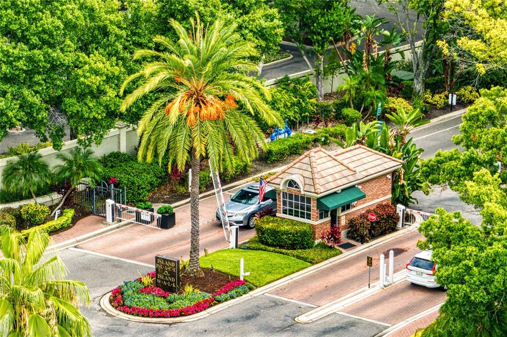 An aerial view of a gated community entrance with a guardhouse, palm tree, and vehicles — 919 NORMANDY TRACE ROAD, TAMPA, FL