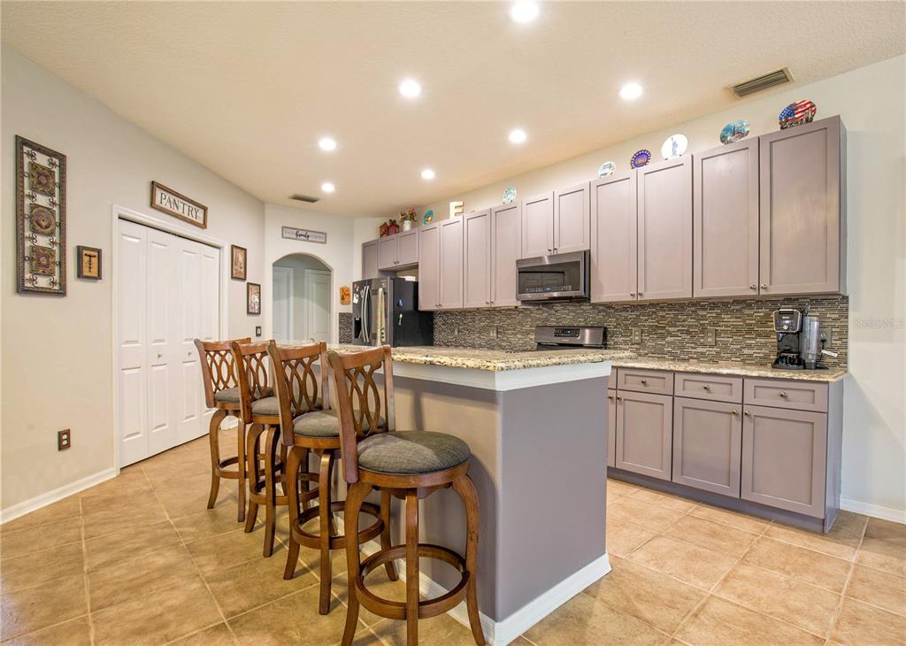 A kitchen features gray cabinets, granite countertops, a breakfast bar with stools, and tile flooring — 1422 TAWNYBERRY COURT, TRINITY, FL