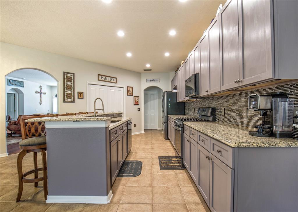 A kitchen features gray cabinetry, granite countertops, a tile backsplash, and a breakfast bar — 1422 TAWNYBERRY COURT, TRINITY, FL