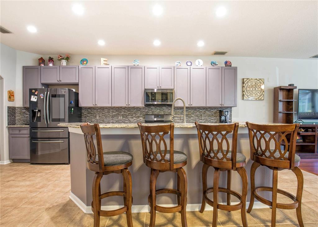 A kitchen features light purple cabinets, a granite countertop, and four wooden bar stools — 1422 TAWNYBERRY COURT, TRINITY, FL
