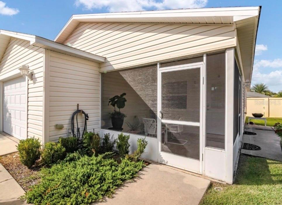 A beige house exterior features a screened-in porch, a garage, and a small landscaped garden — 1037 RIDGEVILLE ROAD, THE VILLAGES, FL