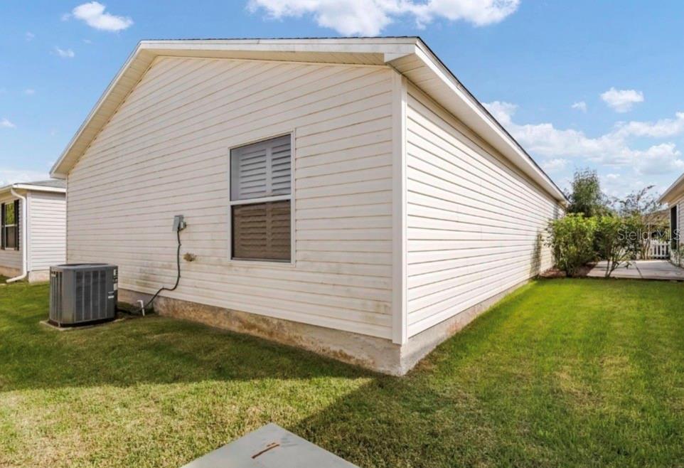 The exterior side view of a house features light-colored vinyl siding and an air conditioning unit — 1037 RIDGEVILLE ROAD, THE VILLAGES, FL