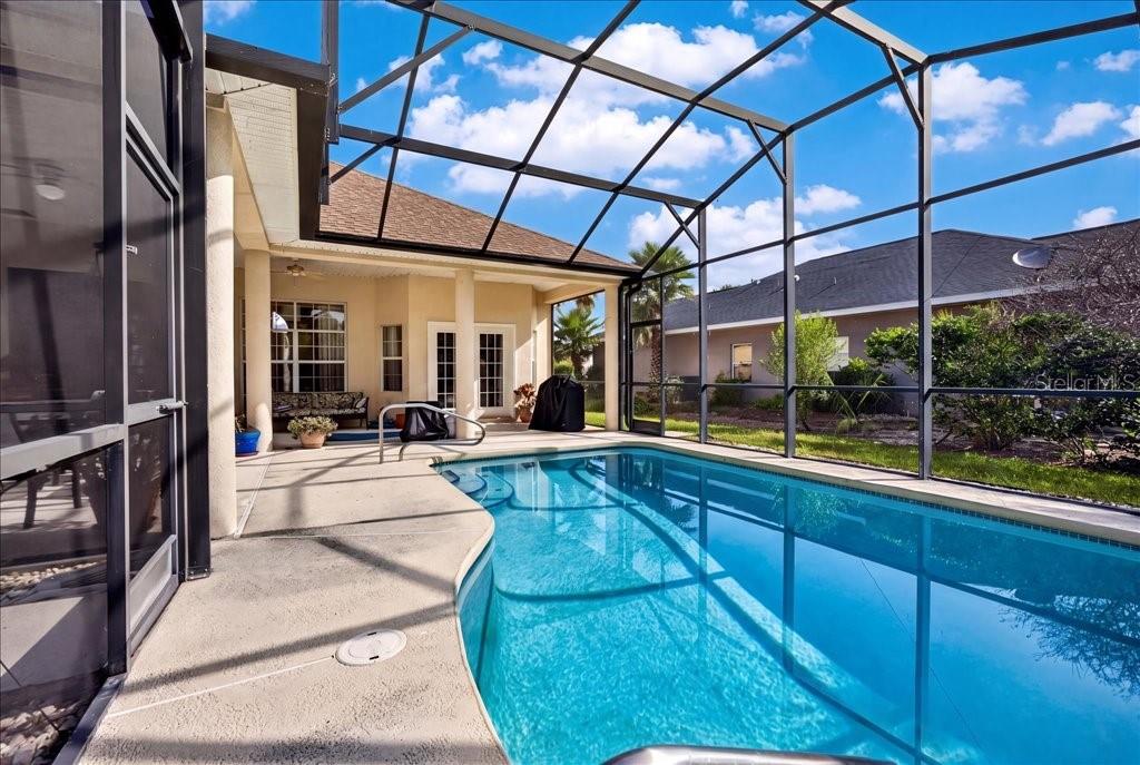 A swimming pool with a screen enclosure sits on a patio next to a house — 10 BEACHSIDE DRIVE, PALM COAST, FL