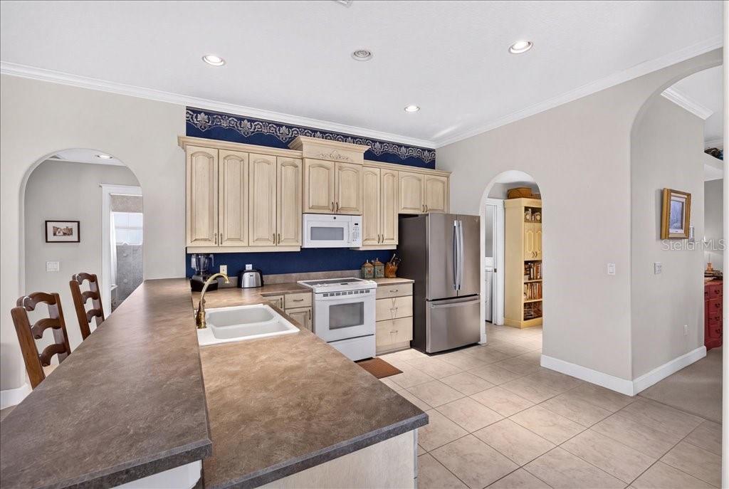 A kitchen features light-colored cabinets, dark countertops, stainless steel appliances, and a blue backsplash — 10 BEACHSIDE DRIVE, PALM COAST, FL