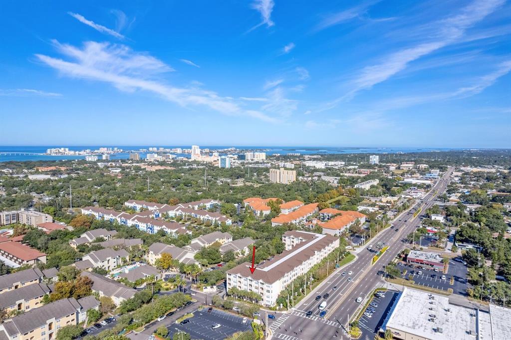 An aerial view shows a multi-story apartment complex situated near a busy road and coastline — 1216 S MISSOURI AVENUE UNIT 226, CLEARWATER, FL