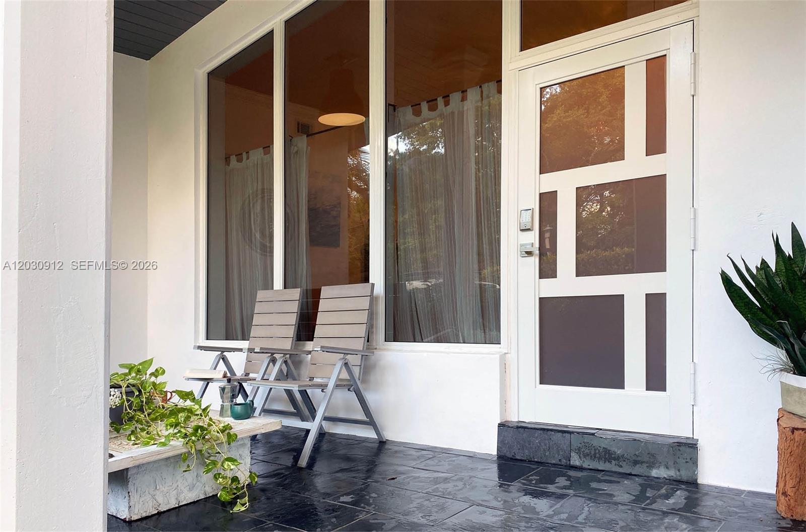 A covered patio features dark stone flooring, two folding chairs, and a modern glass-paneled door — 1030 NE 81st St, Miami FL 33138, MIAMI, FL