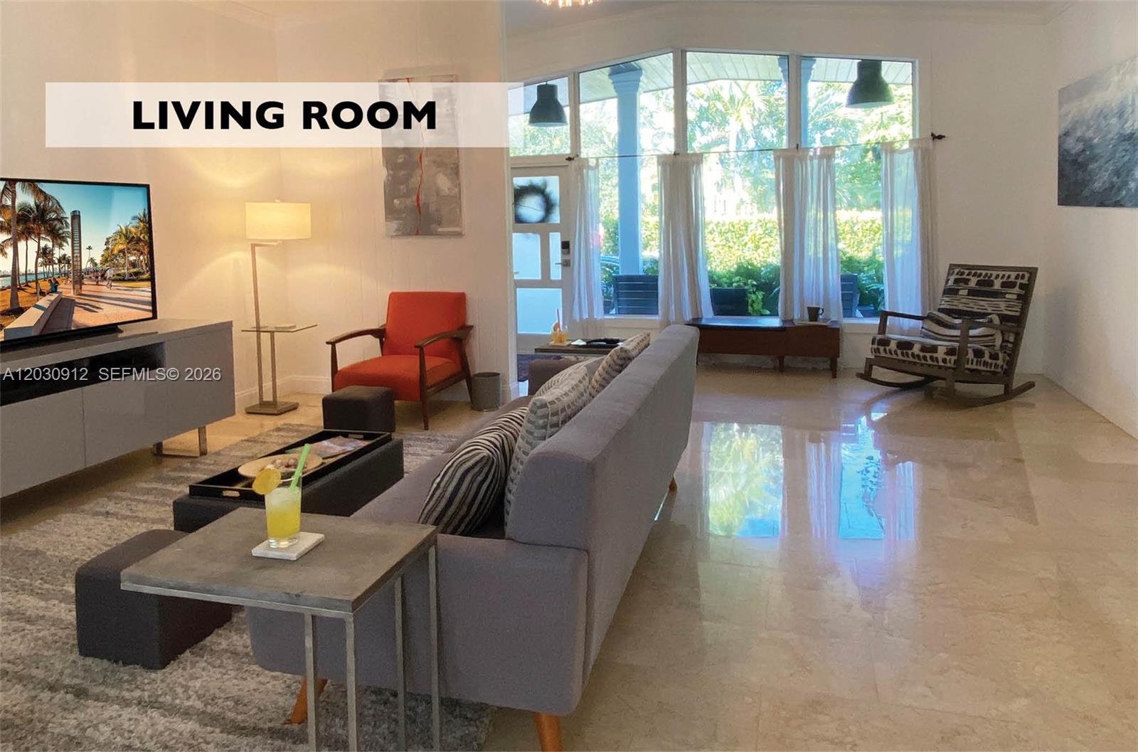 A living room features a grey sofa, an orange chair, a rocking chair, and large windows — 1030 NE 81st St, Miami FL 33138, MIAMI, FL