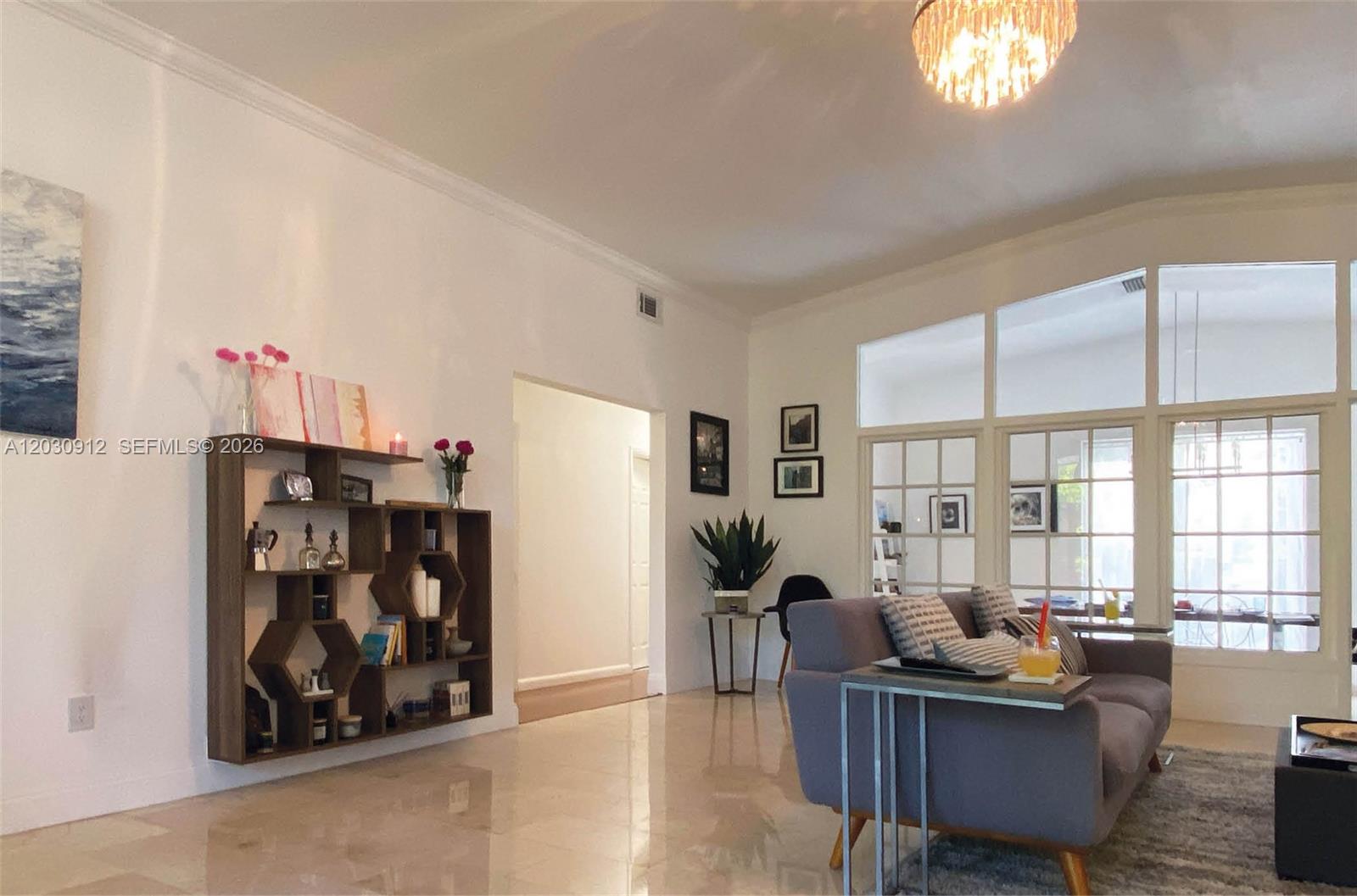 A living room features a grey sofa, a geometric wall shelf, and large glass-paned doors — 1030 NE 81st St, Miami FL 33138, MIAMI, FL