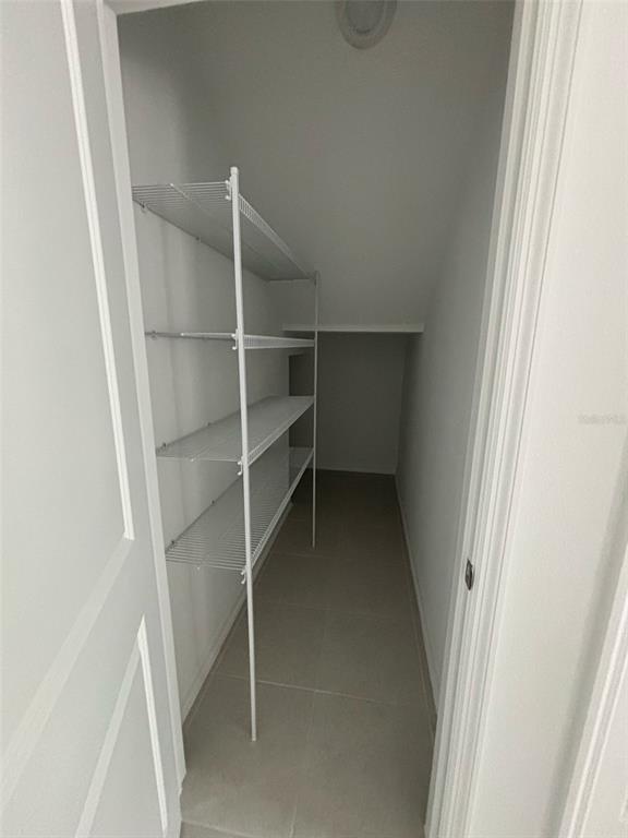 A narrow walk-in closet features white wire shelving, light-colored tile flooring, and white walls — 1996 TOHOQUA BOULEVARD, KISSIMMEE, FL