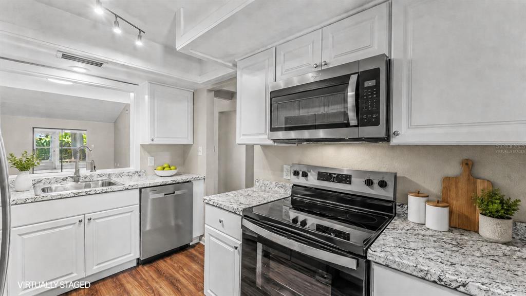 A kitchen features white cabinets, granite countertops, stainless steel appliances, and a view into another room — 2025 SYLVESTER RD UNIT C1, LAKELAND, FL