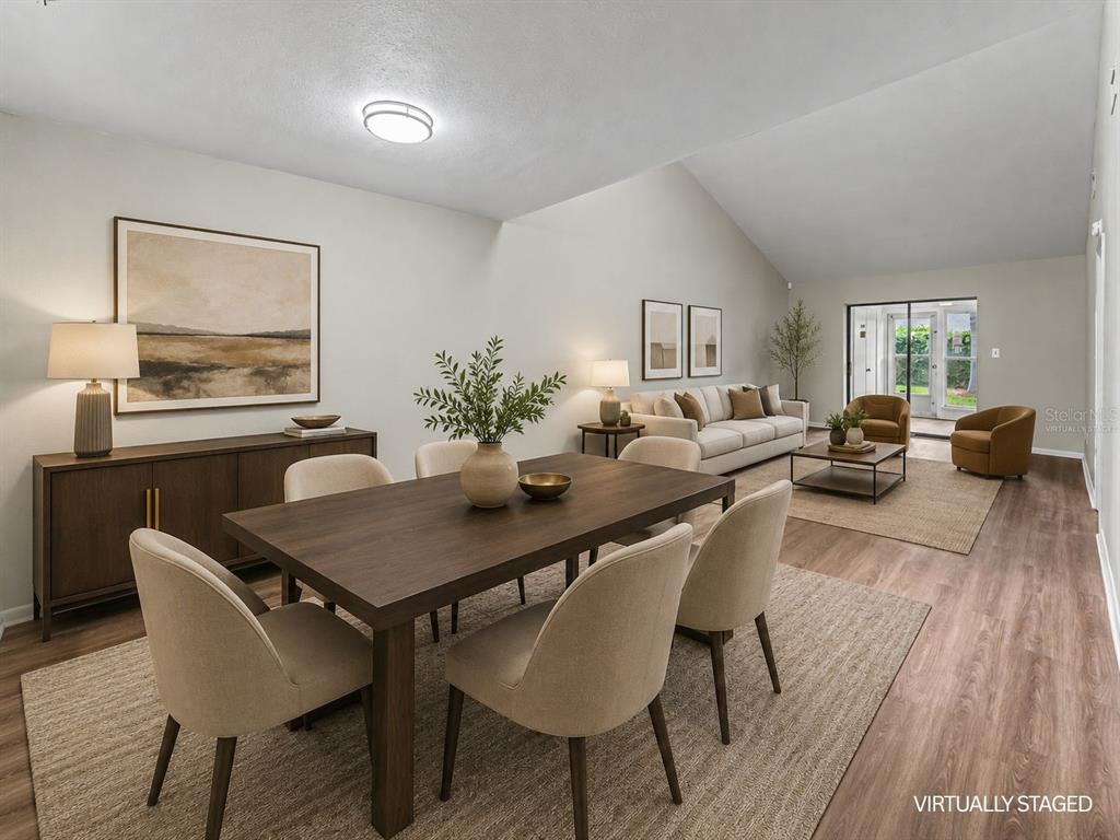 A virtually staged open-concept living and dining area with vaulted ceilings and wood-look flooring — 2025 SYLVESTER RD UNIT C1, LAKELAND, FL