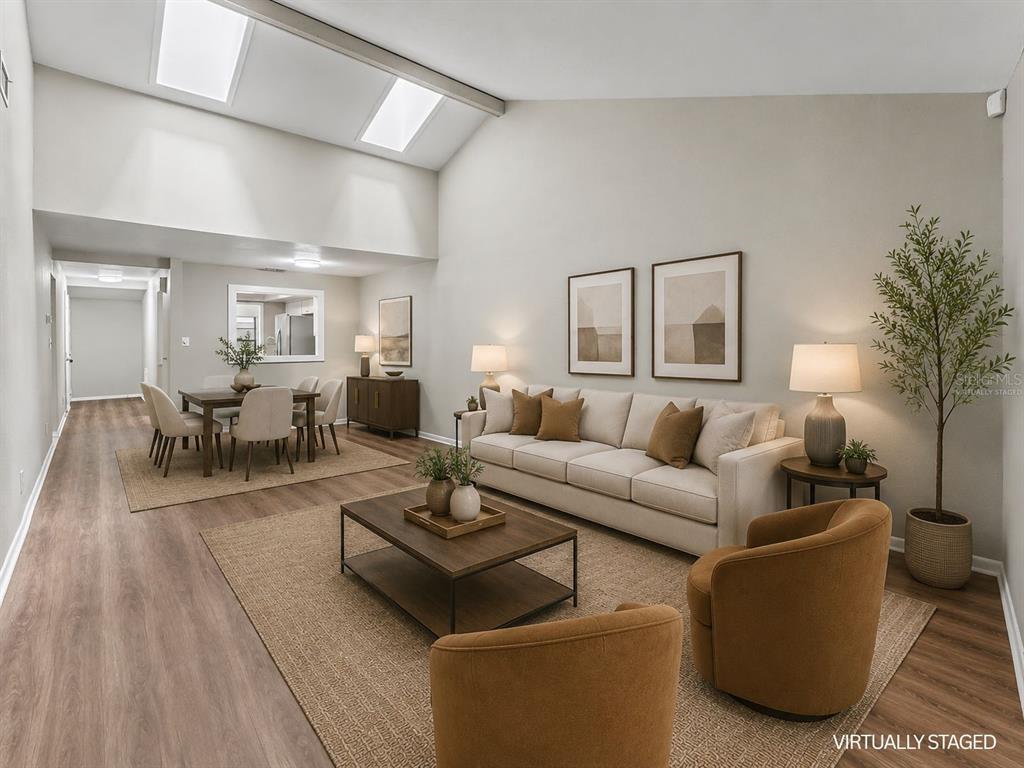 A virtually staged living and dining room with vaulted ceilings, skylights, and wood-look flooring — 2025 SYLVESTER RD UNIT C1, LAKELAND, FL