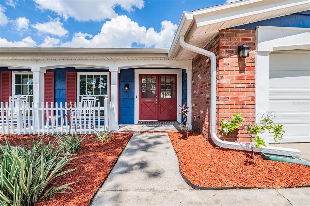 A red double front door is centered on the exterior of a brick and blue house — 3849 CLAREMONT DRIVE, NEW PORT RICHEY, FL