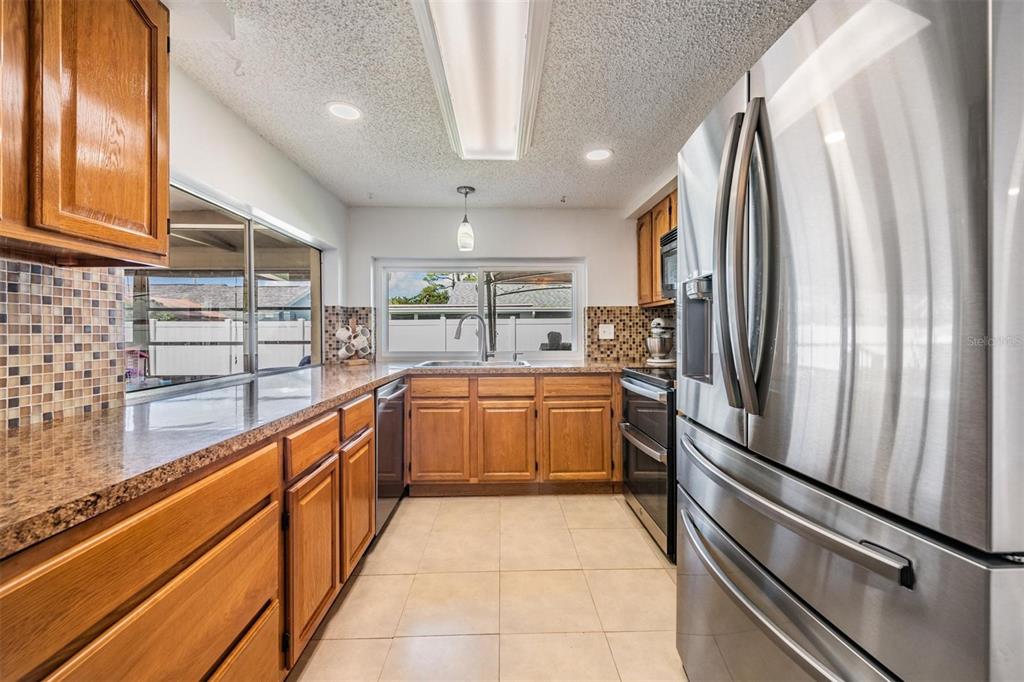 A kitchen features wood cabinets, granite countertops, stainless steel appliances, and a tiled floor — 3849 CLAREMONT DRIVE, NEW PORT RICHEY, FL