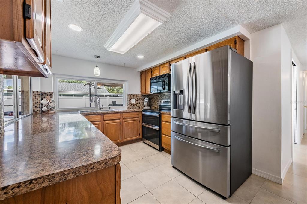 A kitchen features wood cabinets, granite countertops, stainless steel appliances, and a window over the sink — 3849 CLAREMONT DRIVE, NEW PORT RICHEY, FL