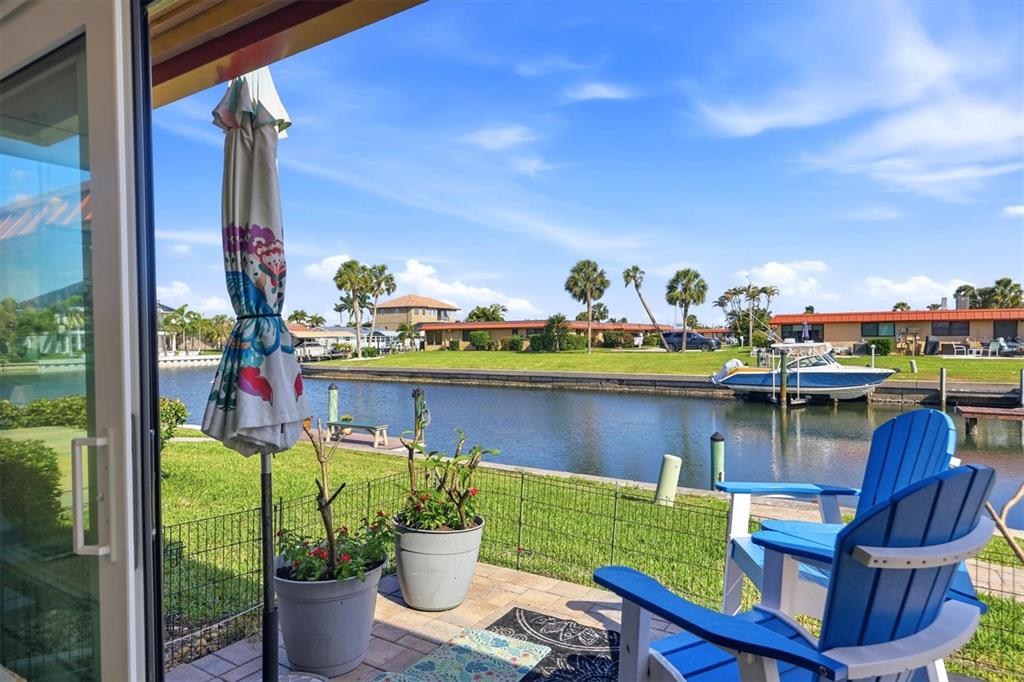 A patio with two blue chairs overlooks a canal with a boat and houses — 9528 ANTIQUA COVE UNIT 9528, BRADENTON, FL