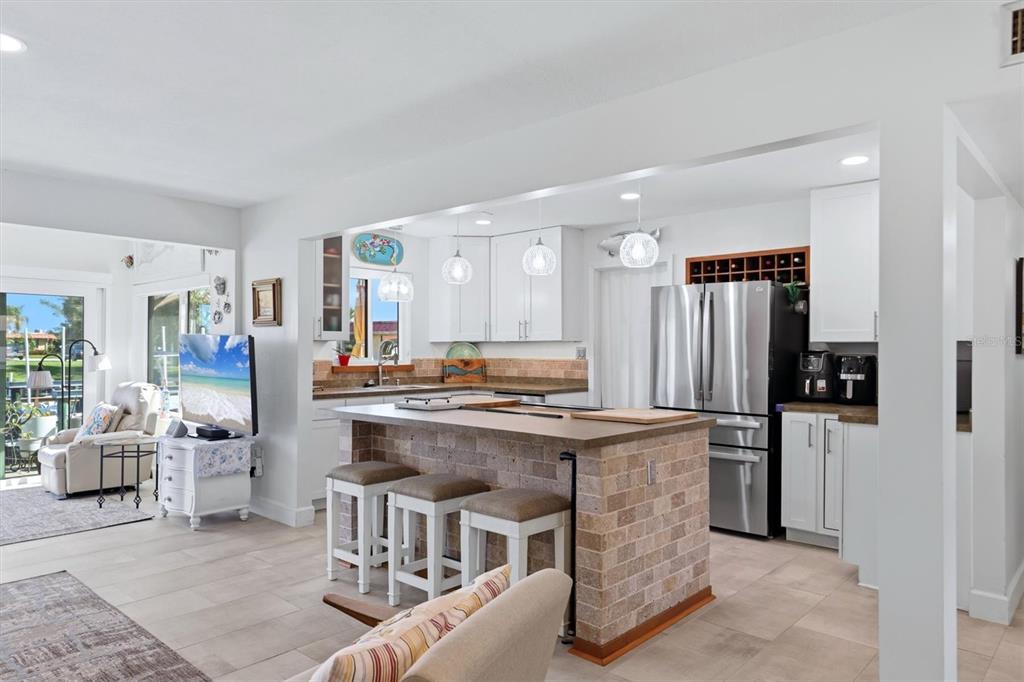 A kitchen with a brick-faced island, white cabinets, and stainless steel appliances opens to living — 9528 ANTIQUA COVE UNIT 9528, BRADENTON, FL