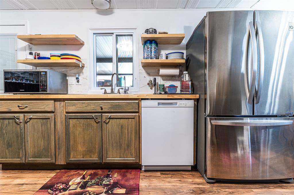 A kitchen features wood cabinets, open shelving, a white dishwasher, and a stainless steel refrigerator — 6450 HOLLYBERRY LANE NE, WINTER HAVEN, FL