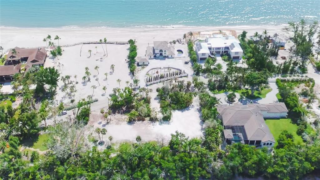 An aerial view shows several luxury beachfront homes surrounded by lush vegetation and sandy terrain — 7825 SANDERLING ROAD, SARASOTA, FL