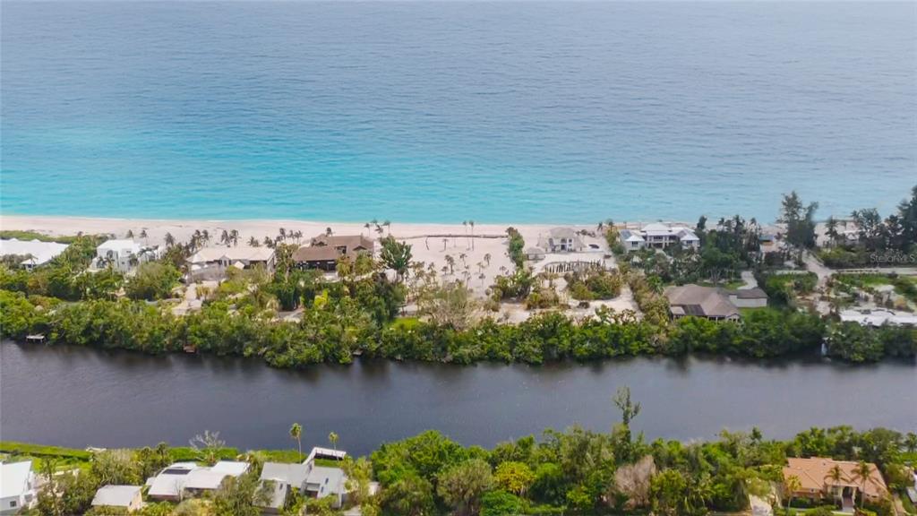 An aerial view shows a coastal property with a beach, houses, and a waterway — 7825 SANDERLING ROAD, SARASOTA, FL
