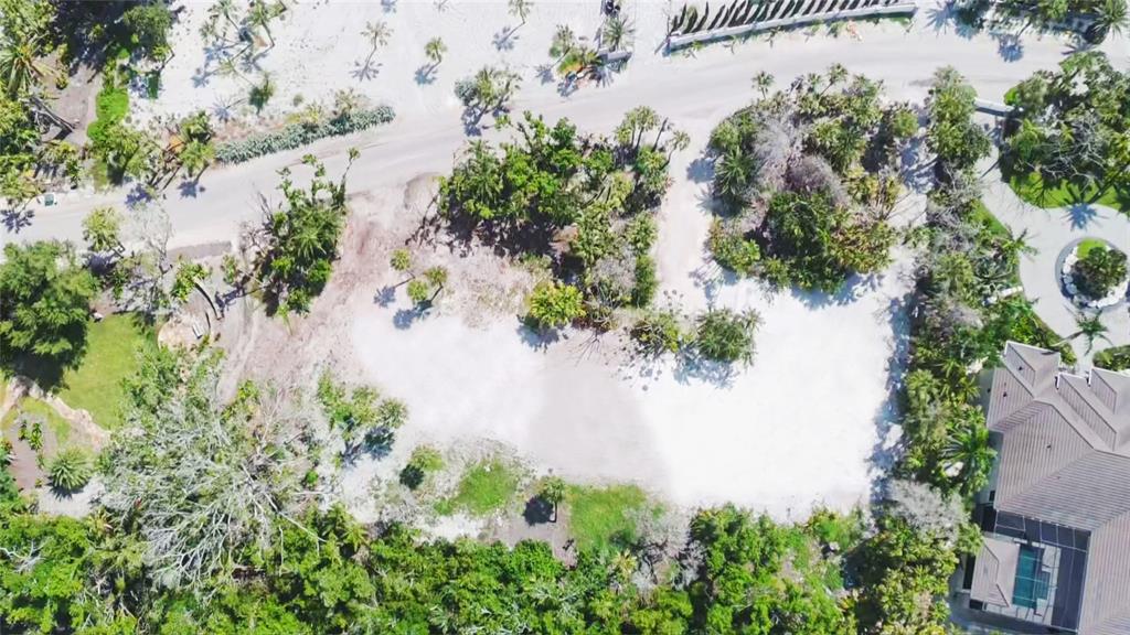 An aerial view shows a cleared, sandy residential lot surrounded by lush trees and vegetation — 7825 SANDERLING ROAD, SARASOTA, FL