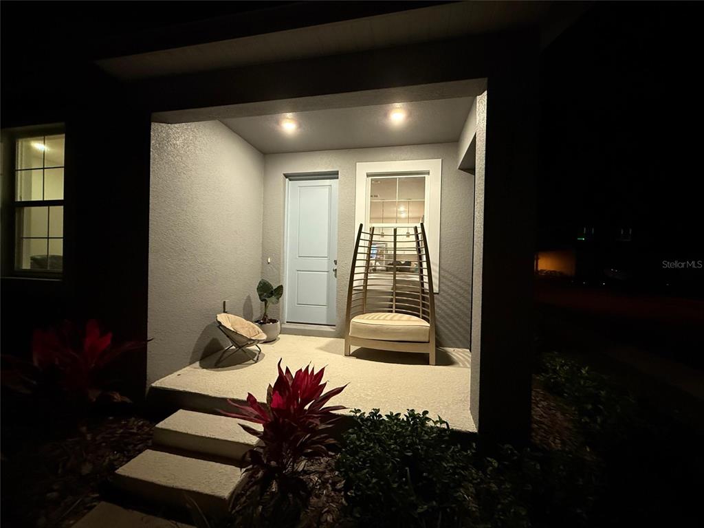 A covered front porch at night features a light blue door and two outdoor chairs — 3323 GRANDE HERON DRIVE, ST CLOUD, FL