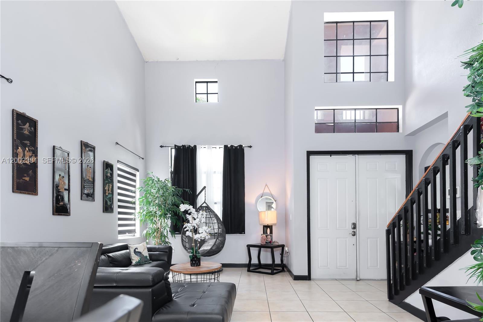 A living room with high ceilings, tile floors, a hanging chair, and a staircase — 685 SE 37th Pl, Homestead FL 33033, HOMESTEAD, FL