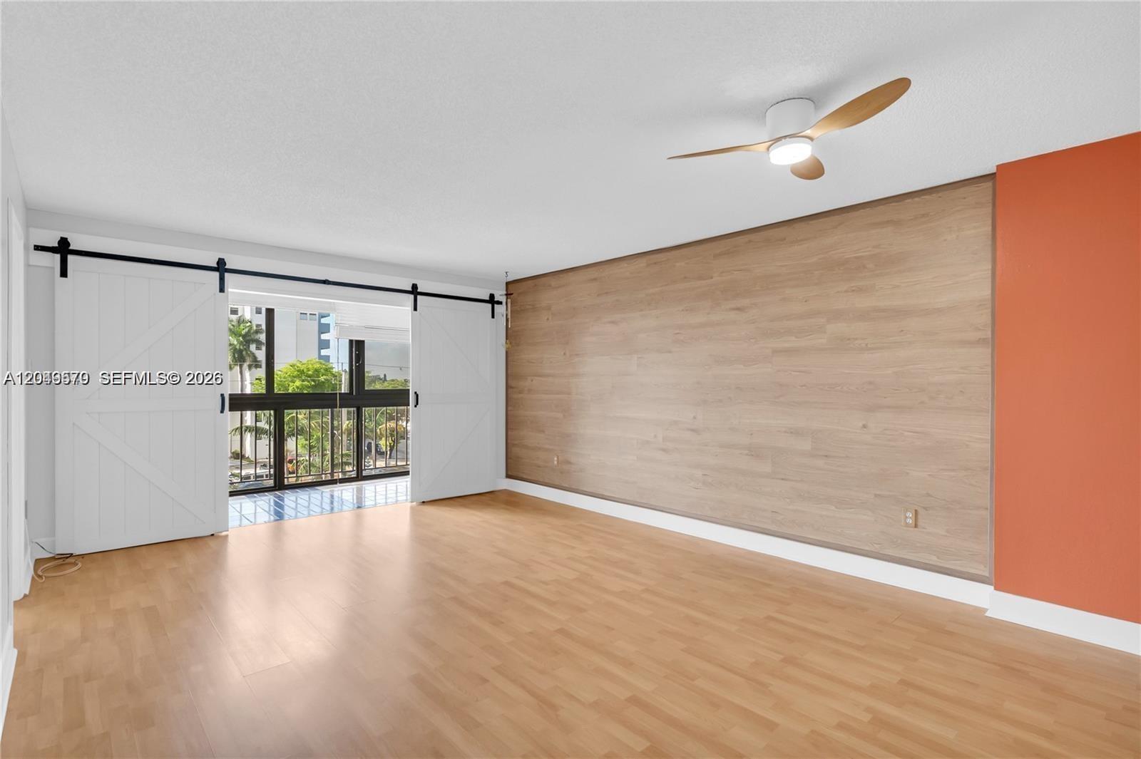 A room features light wood flooring, a wood-paneled accent wall, and white sliding barn doors — 5055 NW 7th St # 504, Miami FL 33126, MIAMI, FL