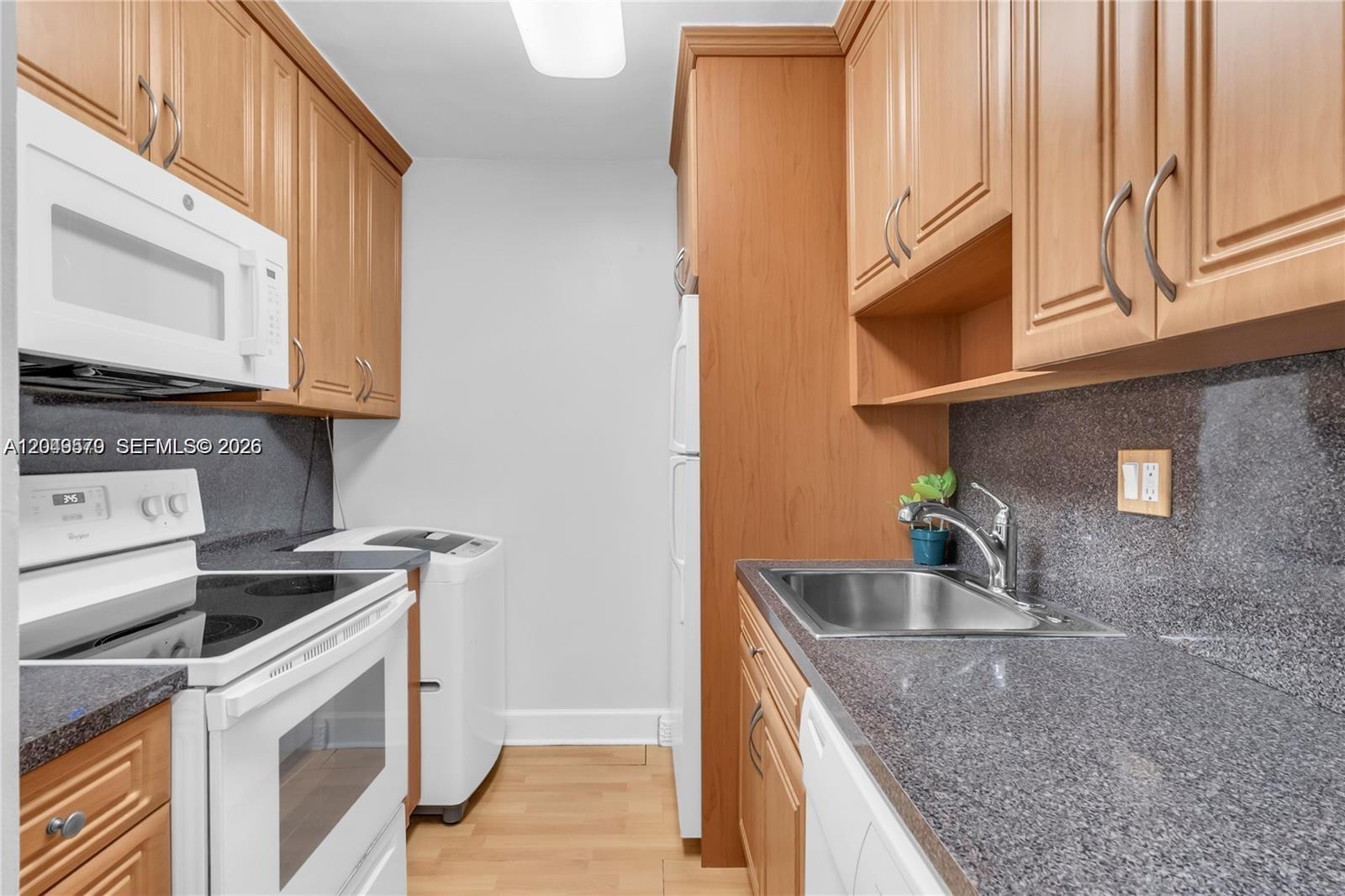 A compact kitchen features wood cabinets, granite countertops, a white stove, and a laundry machine — 5055 NW 7th St # 504, Miami FL 33126, MIAMI, FL
