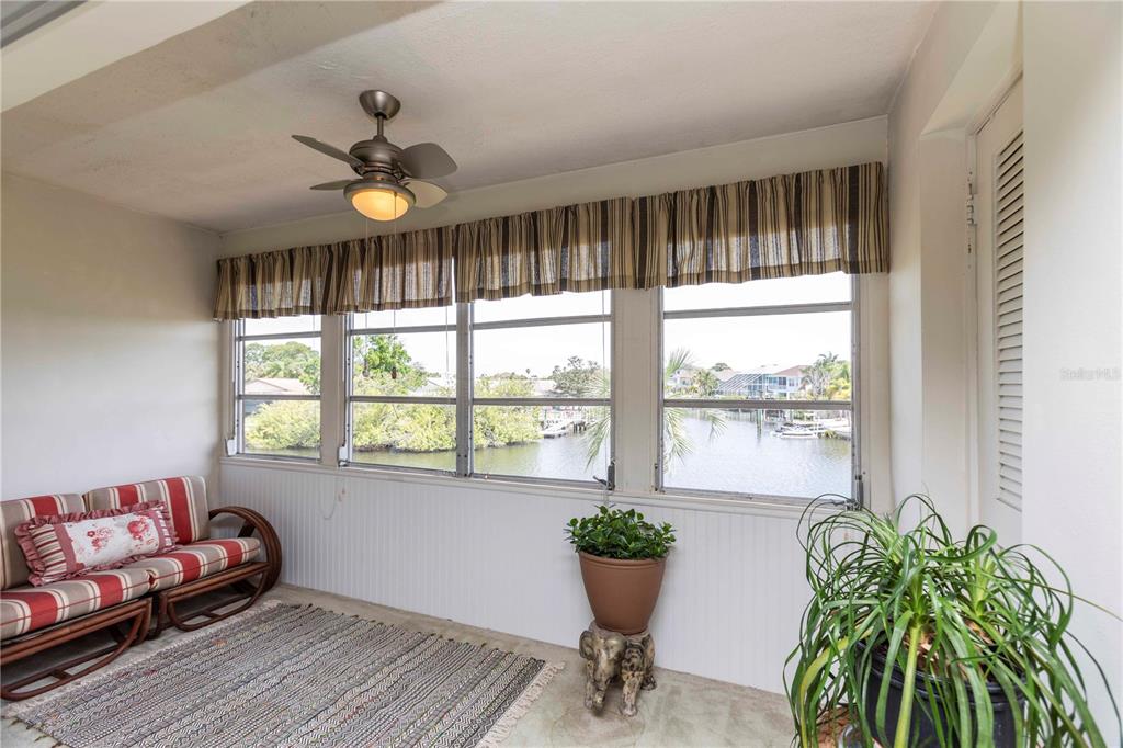 A sunroom features a striped sofa, a ceiling fan, and large windows overlooking a canal — 4609 MARINE PARKWAY UNIT 203, NEW PORT RICHEY, FL