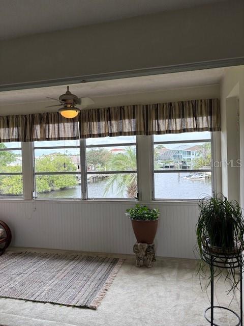 A sunroom features large windows overlooking a canal, a ceiling fan, and a potted plant — 4609 MARINE PARKWAY UNIT 203, NEW PORT RICHEY, FL