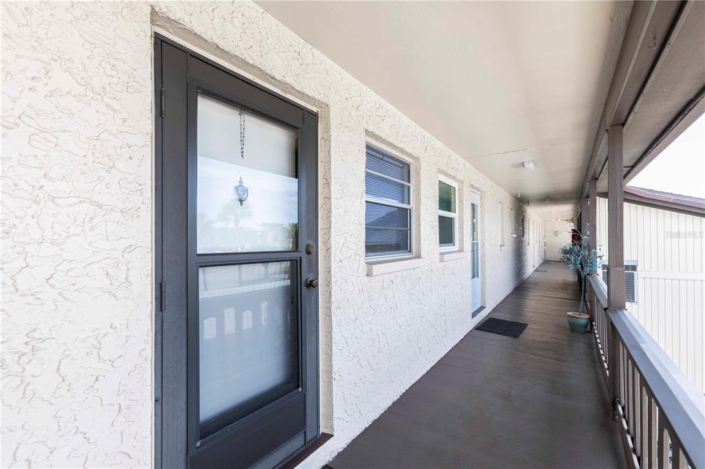 An exterior view of a covered apartment balcony with a dark screen door and windows — 4609 MARINE PARKWAY UNIT 203, NEW PORT RICHEY, FL
