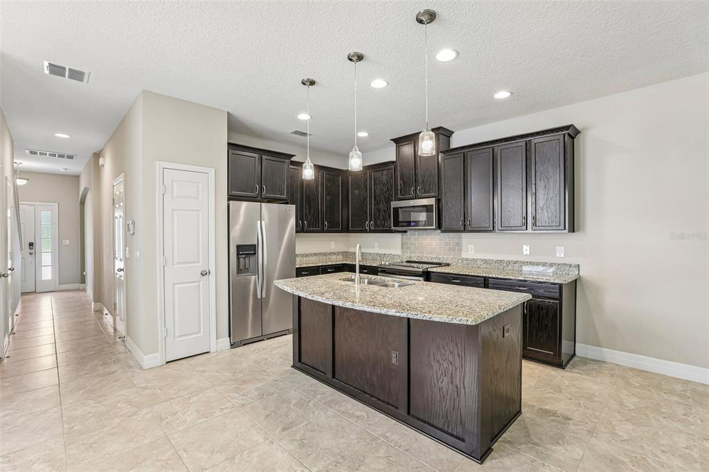A kitchen features dark wood cabinets, granite countertops, a central island, and stainless steel appliances — 198 MITCHELL CREEK WAY, OVIEDO, FL