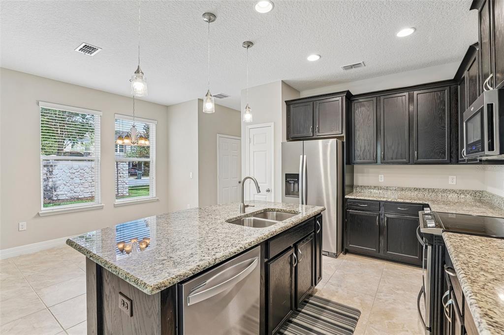 A kitchen features dark wood cabinets, granite countertops, a center island, and stainless steel appliances — 198 MITCHELL CREEK WAY, OVIEDO, FL