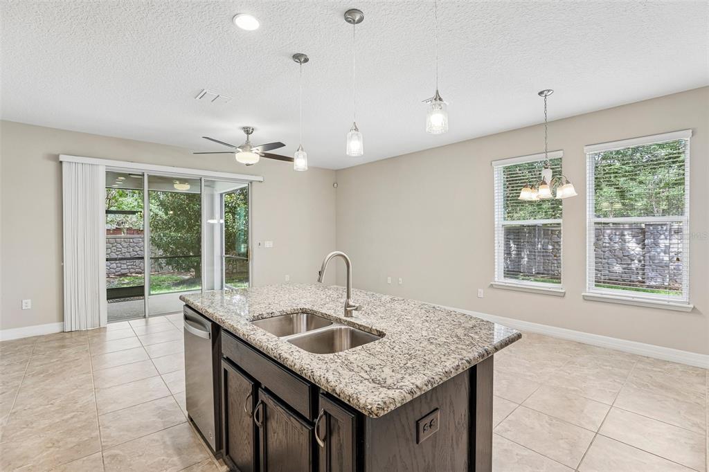 A kitchen island with a granite countertop and sink sits in a tiled open-concept room — 198 MITCHELL CREEK WAY, OVIEDO, FL