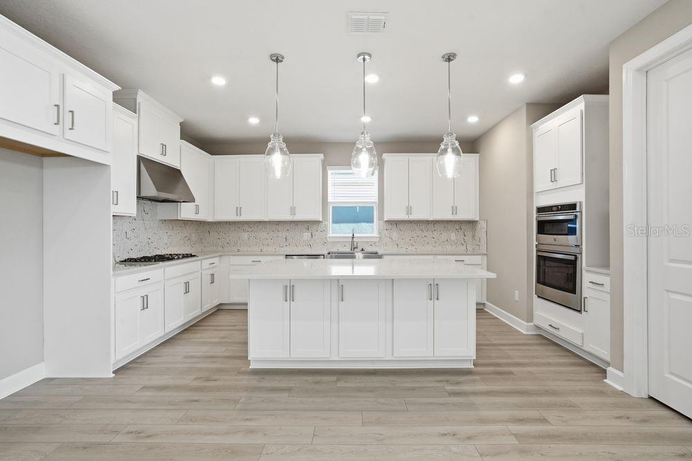 A modern kitchen features white cabinetry, a central island, stainless steel appliances, and wood-look flooring — 7727 CASPIAN STREET, PALMETTO, FL