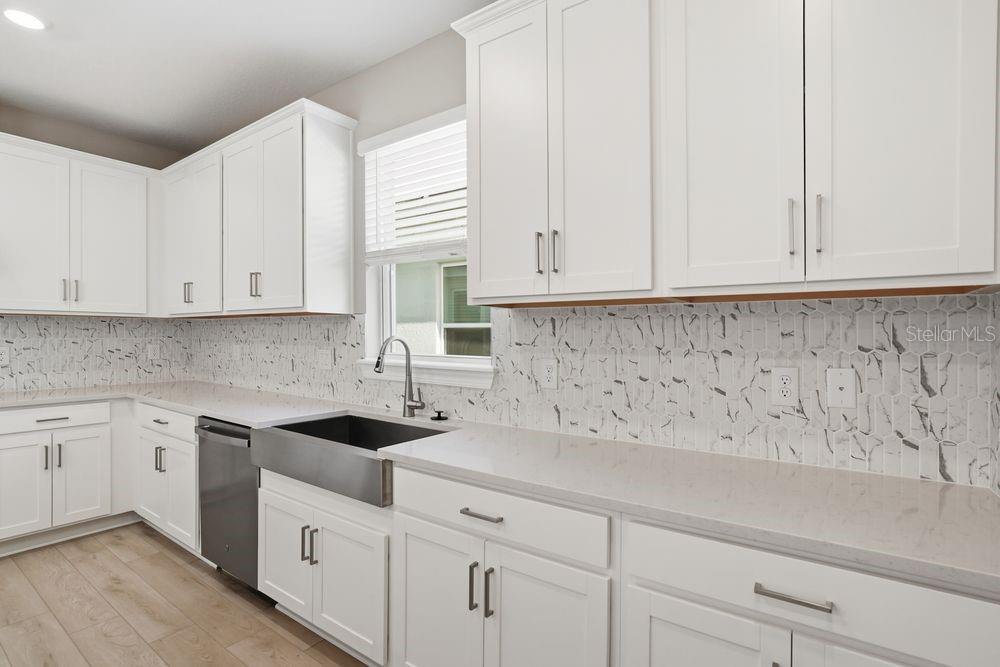 A kitchen features white cabinets, a farmhouse sink, quartz countertops, and a marble-patterned tile backsplash — 7727 CASPIAN STREET, PALMETTO, FL