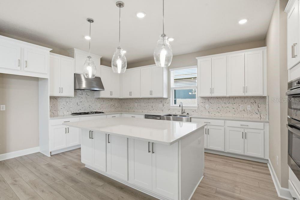 A modern kitchen features white cabinetry, a large central island, and light wood-look flooring — 7727 CASPIAN STREET, PALMETTO, FL