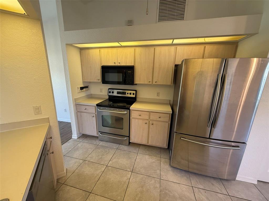 A kitchen features light wood cabinets, stainless steel appliances, and beige tile flooring — 4054 ALLURE LANE, NORTH PORT, FL