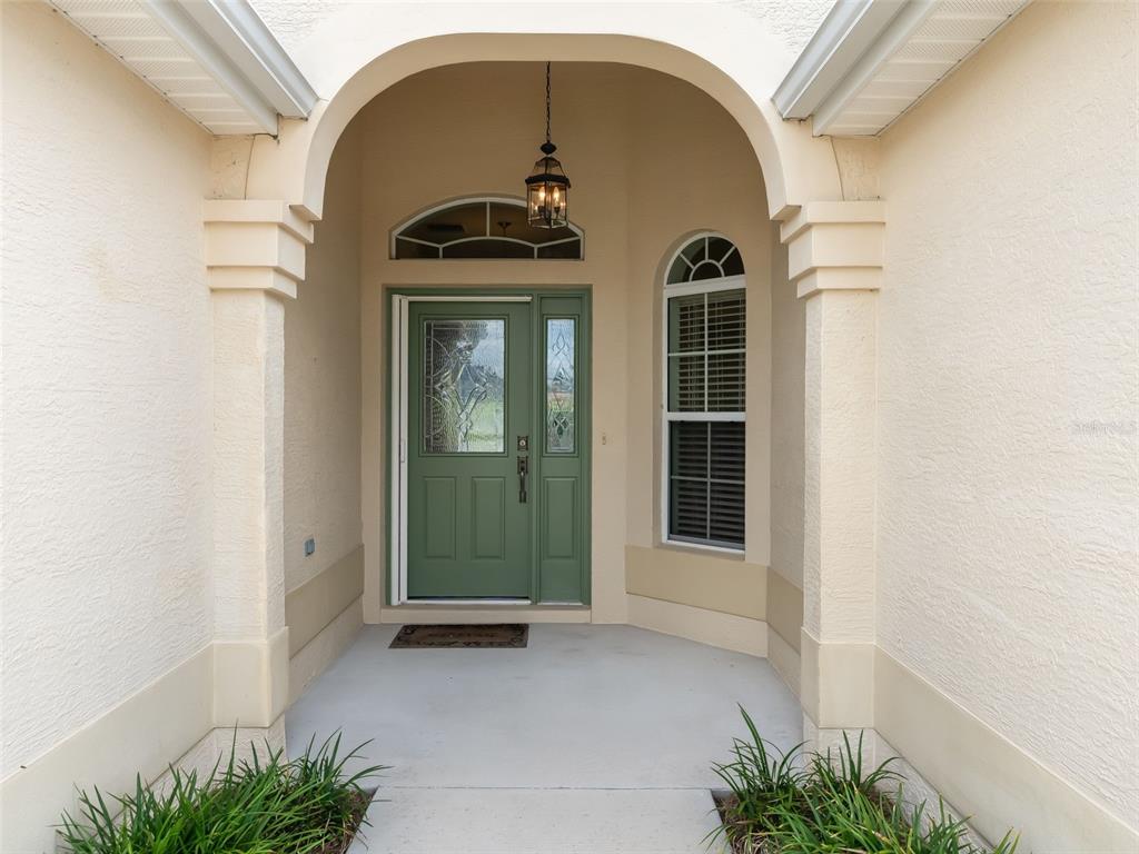 A covered entryway features a green front door with glass panels and an arched window — 2215 TRIGGERFISH RUN, THE VILLAGES, FL