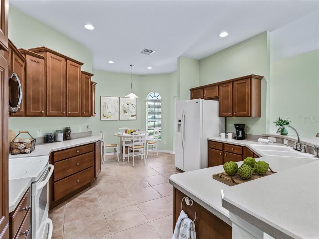 A kitchen with wood cabinets, light countertops, tile floors, and an adjacent dining area — 2215 TRIGGERFISH RUN, THE VILLAGES, FL